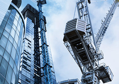 Crane lifting heavy structural bearings outside a tall building on a construction site.